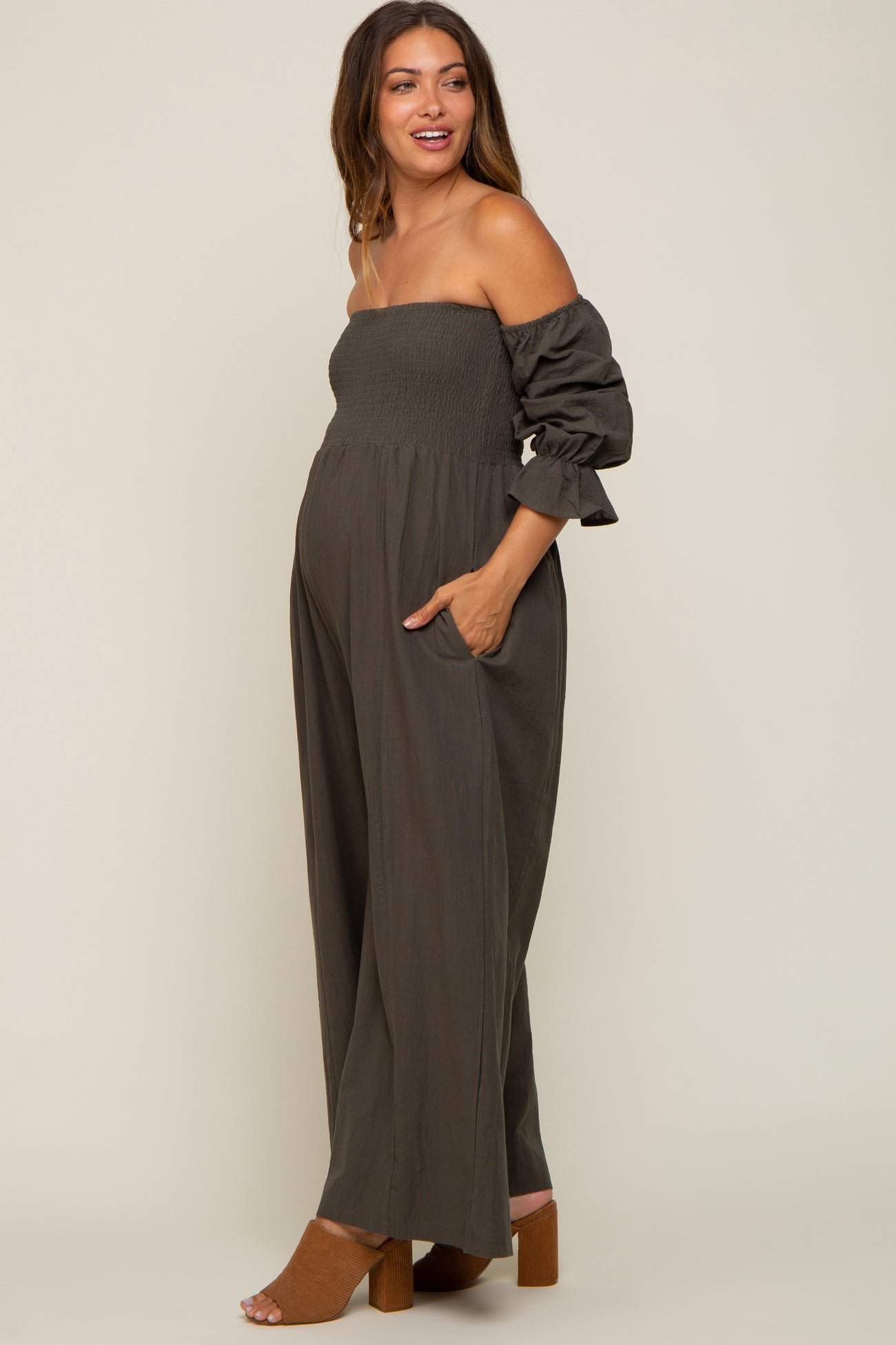woman wearing a dark olive green maternity jumpsuit with off-the-shoulder sleeves and visible baby bump