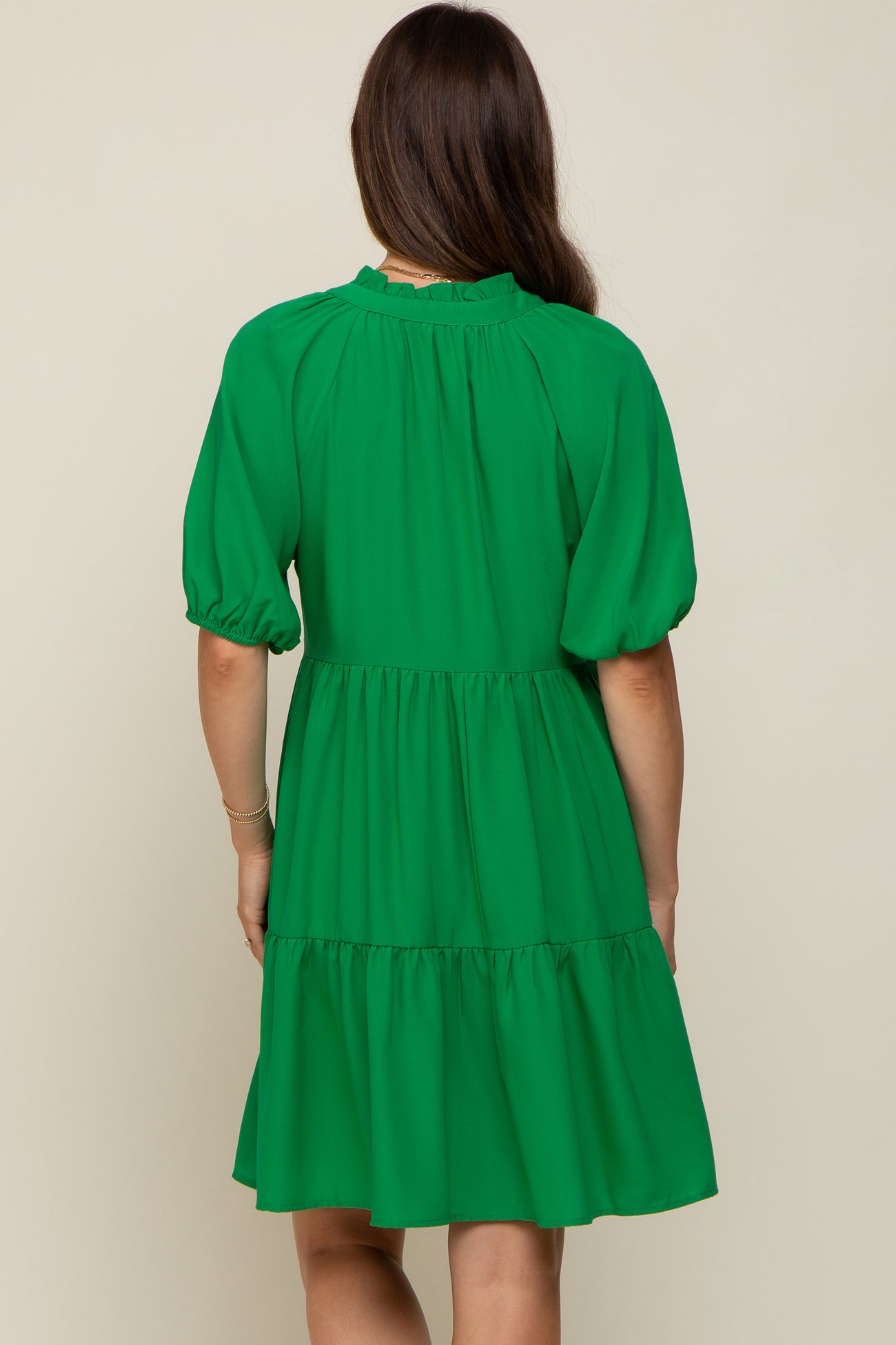 back view of a woman wearing a green tiered mini dress with puff sleeves and a ruffled neckline