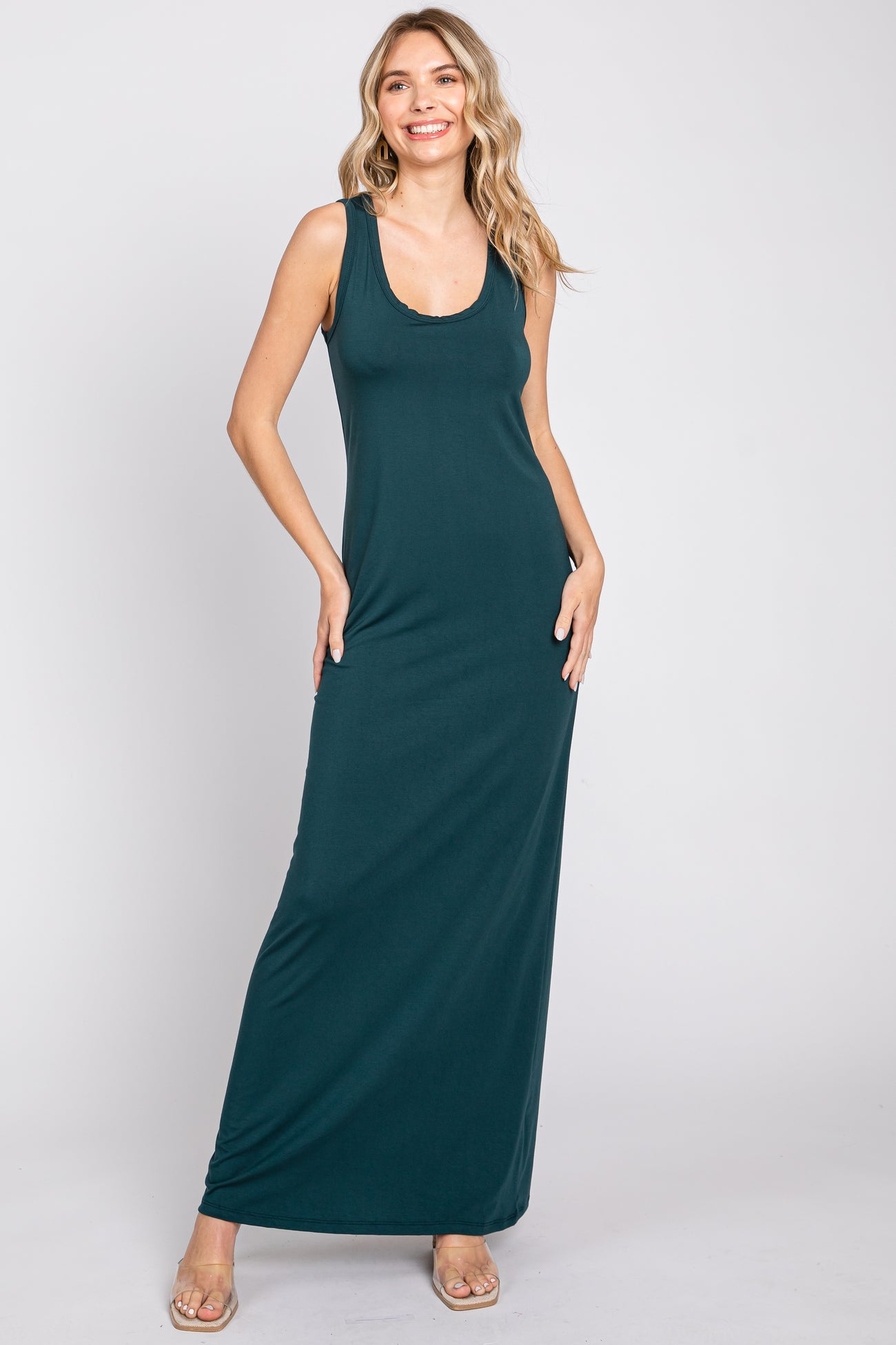 Woman wearing a sleeveless dark green maxi dress with a scoop neckline and clear sandals
