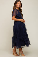woman wearing a navy blue maternity dress with ruffle sleeves and a tiered tulle skirt, holding her baby bump
