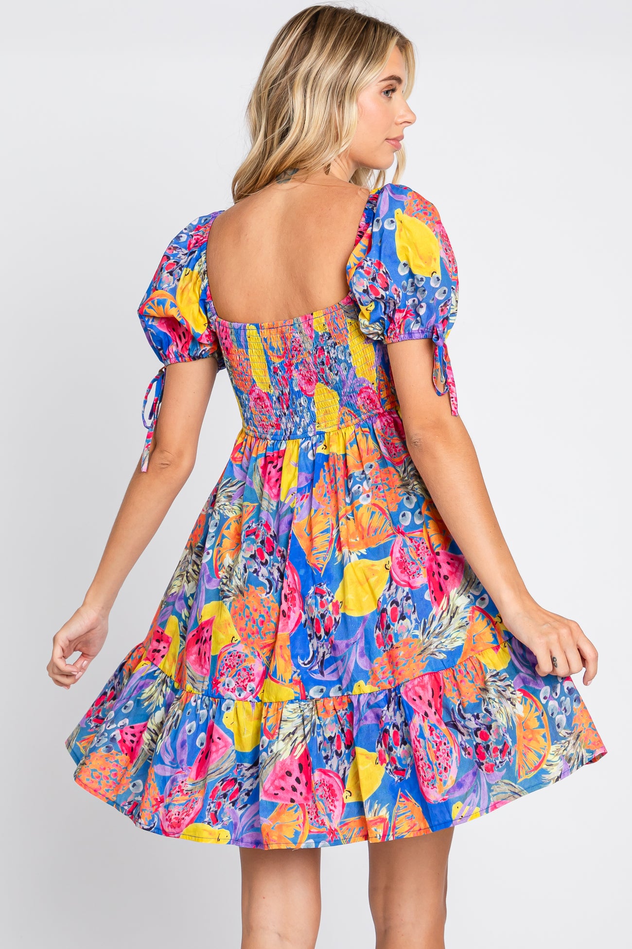 woman wearing a colorful tropical fruit print mini dress with puff sleeves and a smocked back
