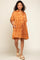 woman wearing an orange short sleeve button-up dress with a playful print and side pockets, standing in casual sandals