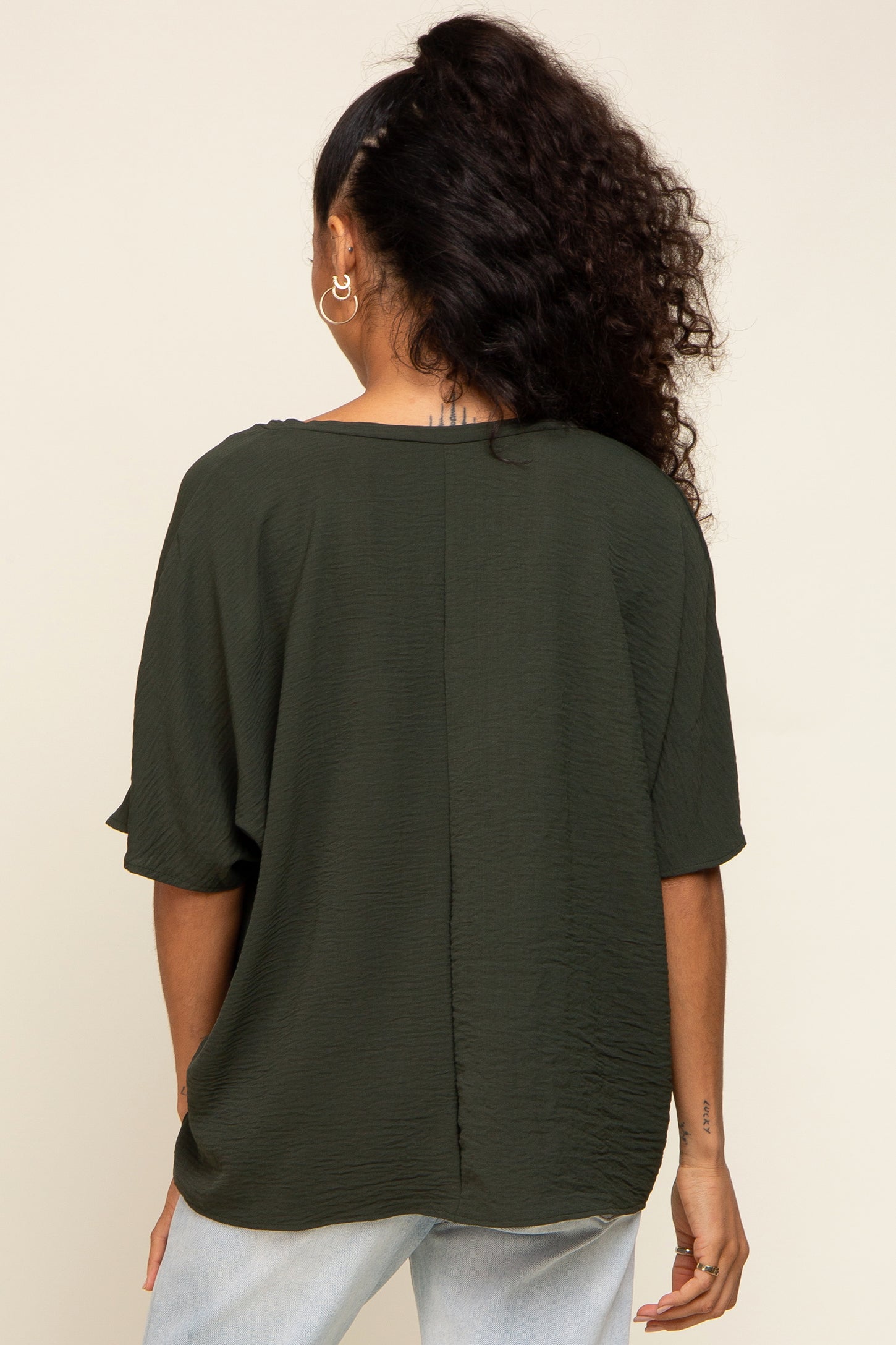 Back view of a woman wearing a dark olive green short sleeve textured blouse and light wash jeans
