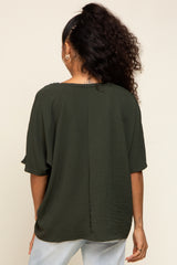 Back view of a woman wearing a dark olive green short sleeve textured blouse and light wash jeans