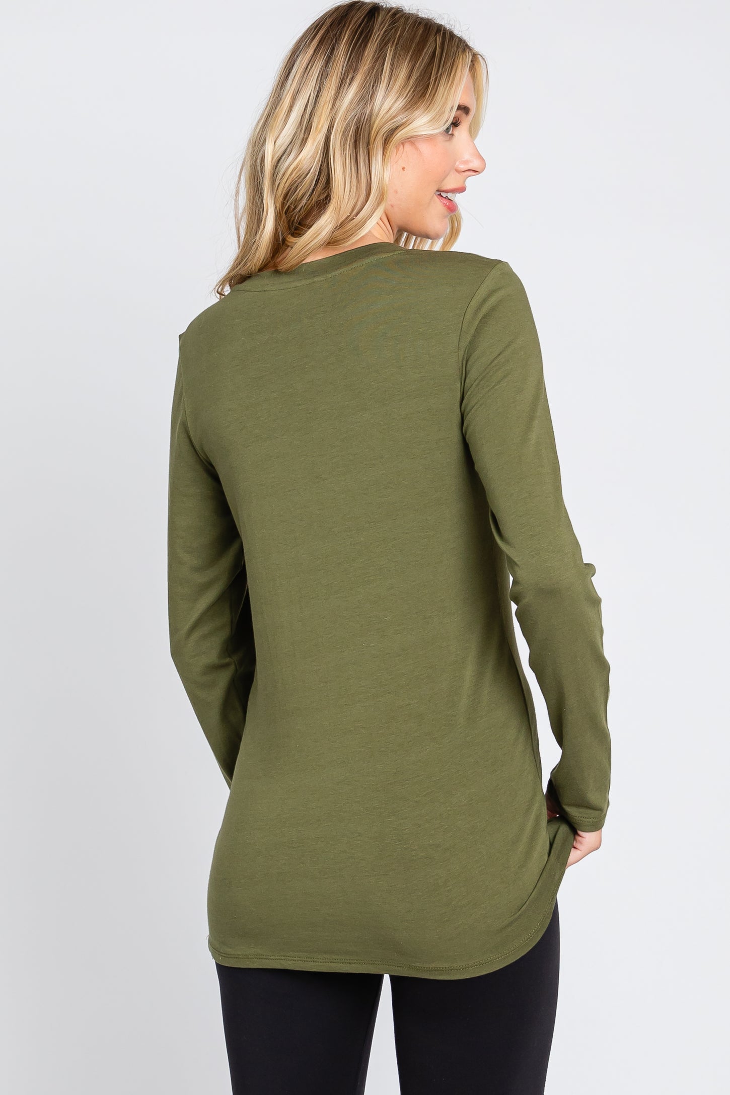woman wearing a long sleeve olive green top, seen from the back, paired with black leggings