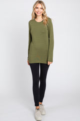 woman wearing an olive green long sleeve top and black leggings, standing with a relaxed pose
