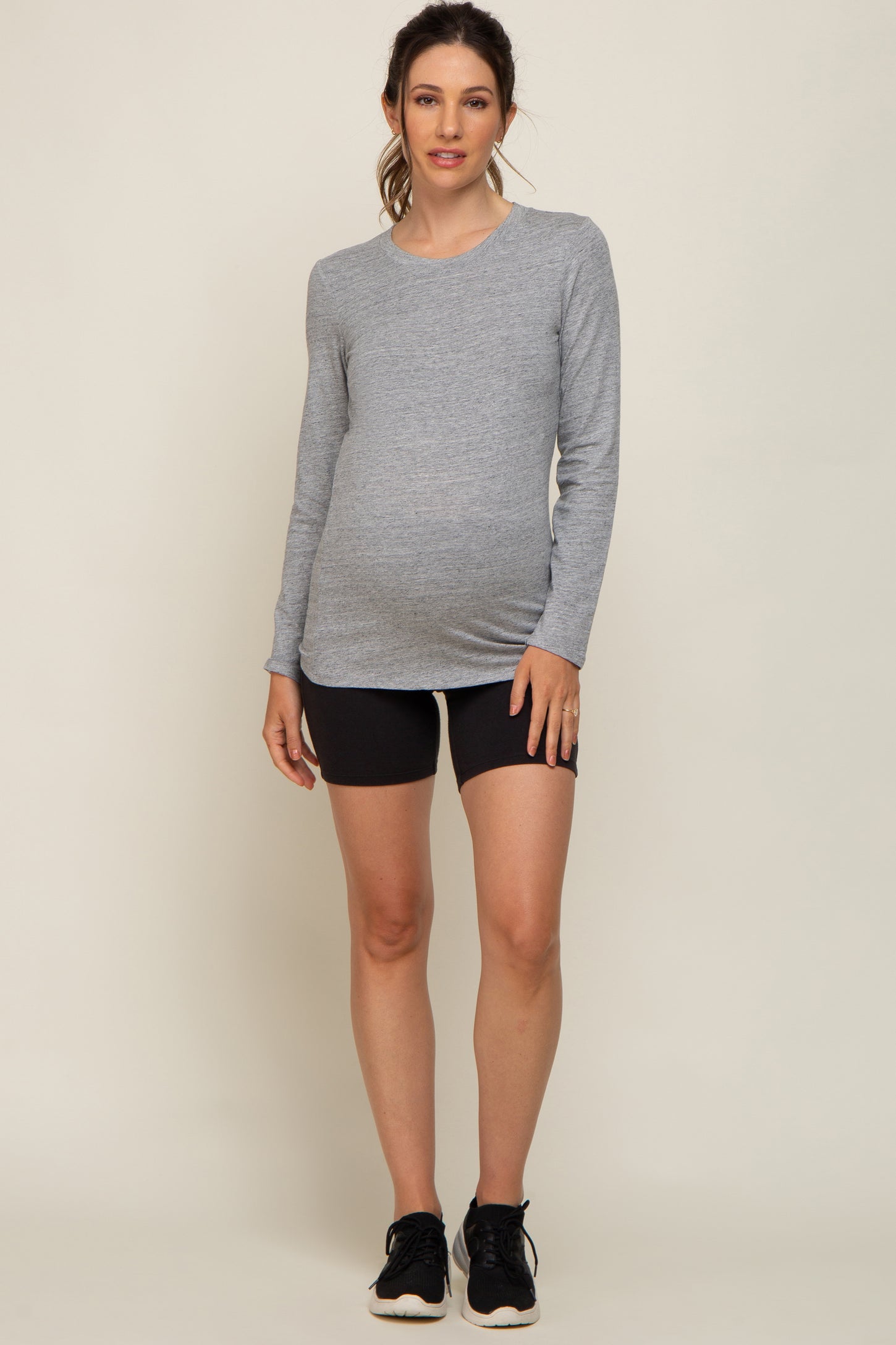 woman wearing a gray long sleeve maternity top and black shorts, showing her baby bump