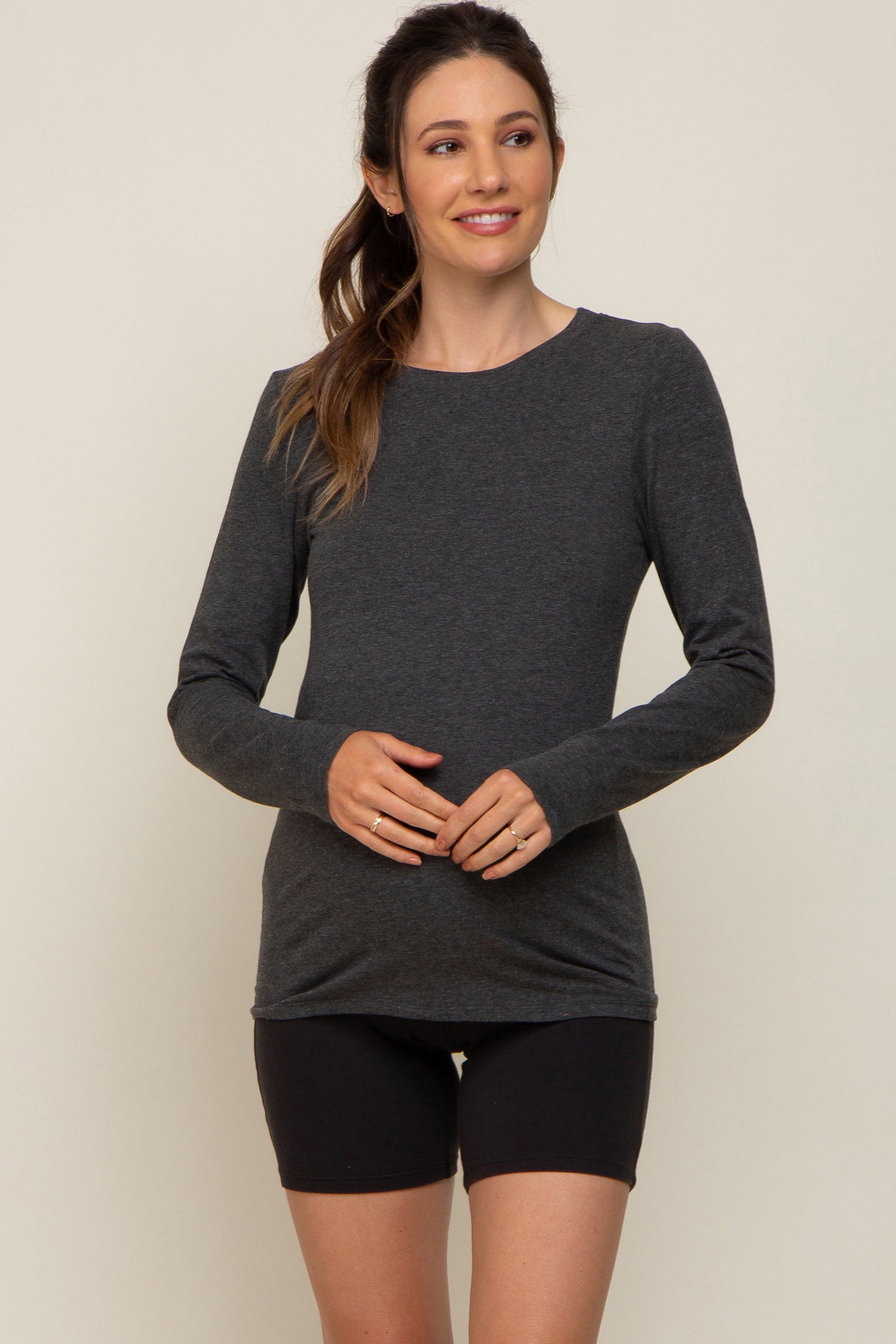 woman wearing a dark gray long sleeve maternity top and showing her baby bump with black shorts