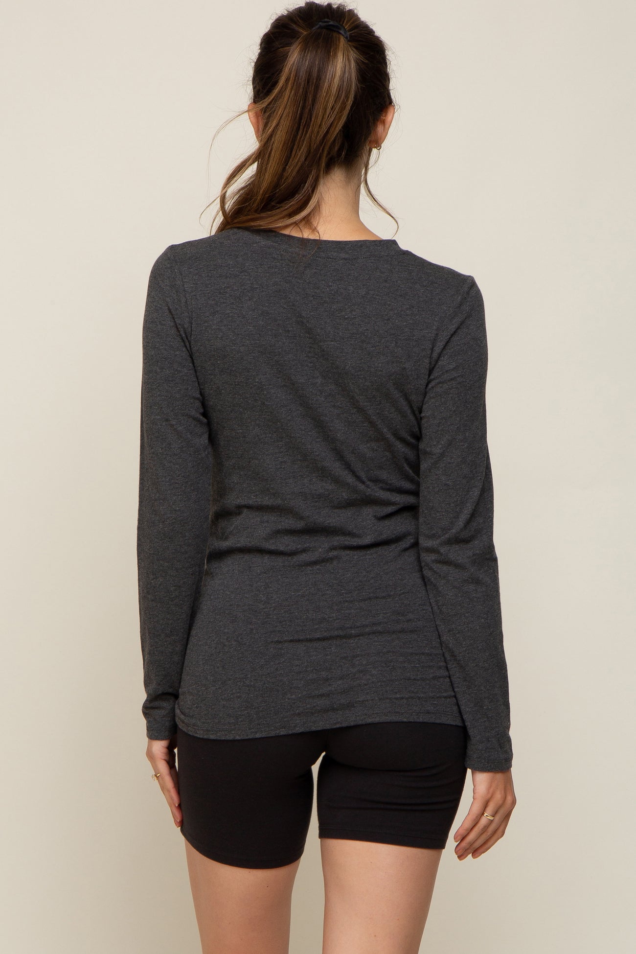 woman wearing a dark gray long sleeve maternity top viewed from the back with black shorts