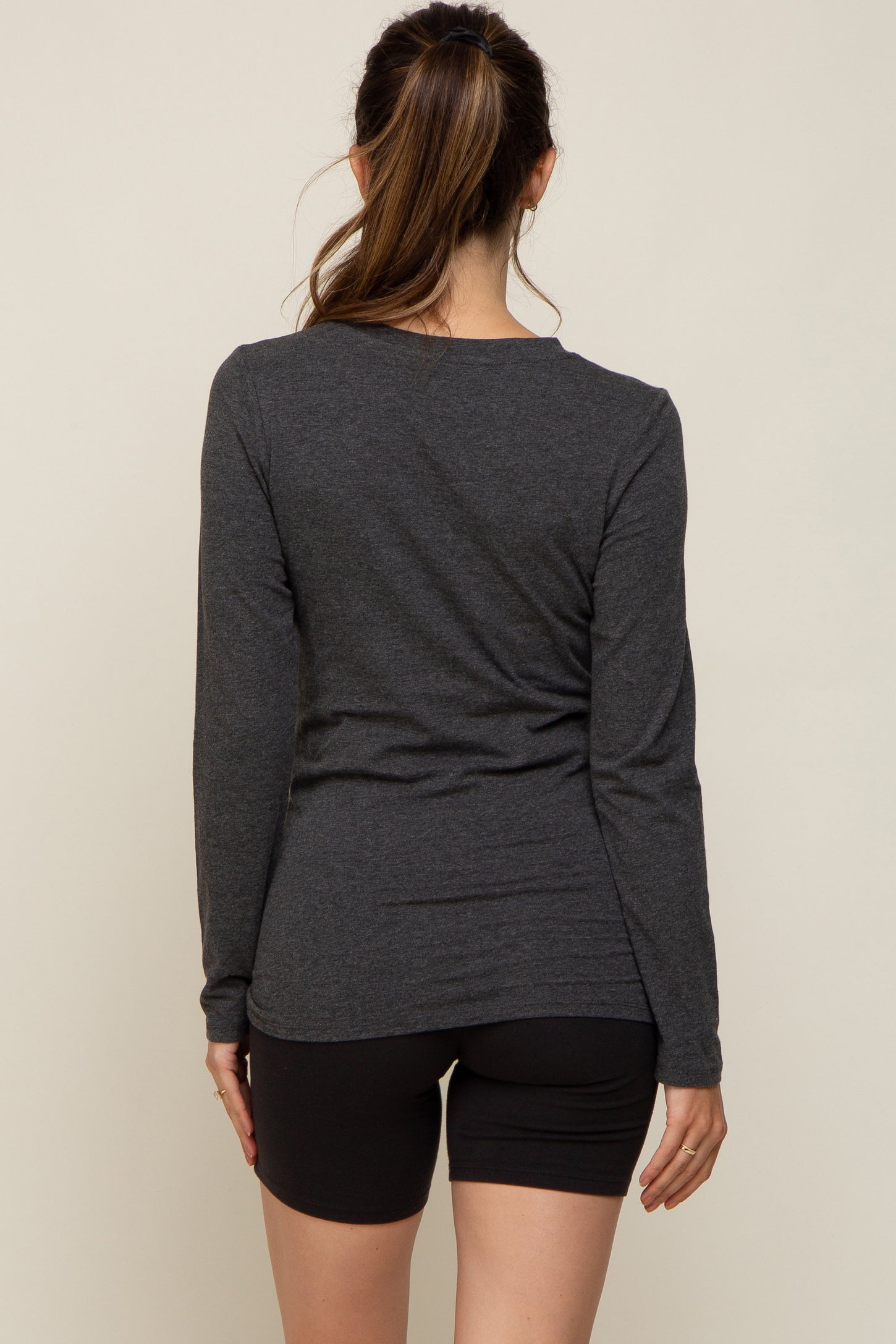 woman wearing a dark gray long sleeve maternity top viewed from the back with black shorts