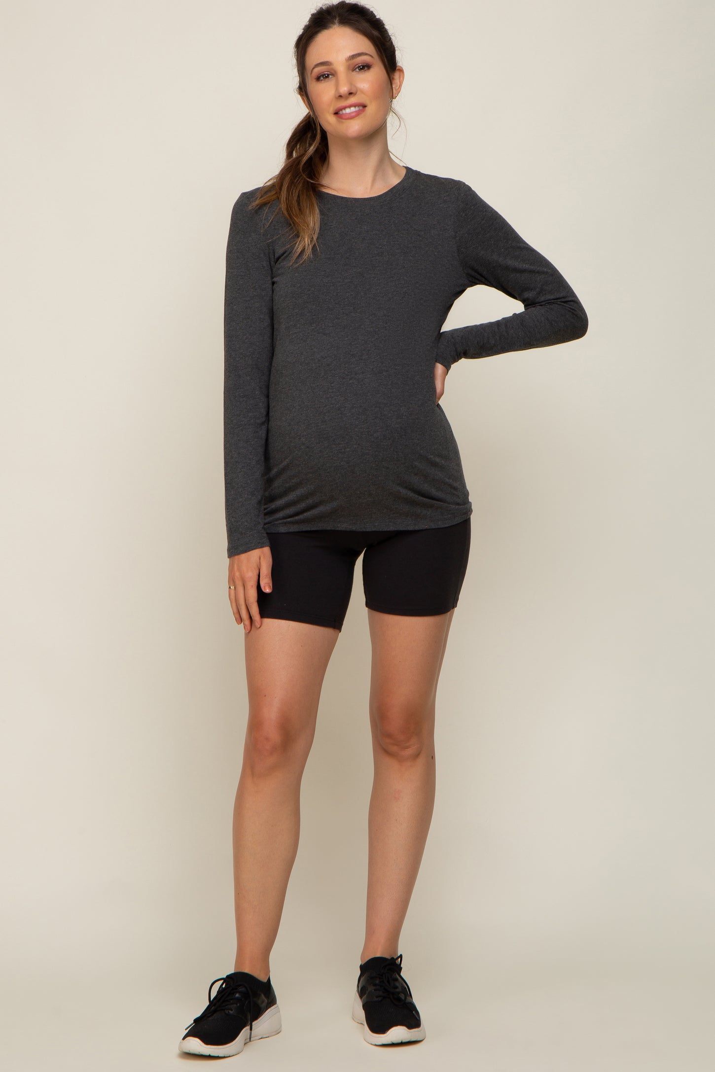 woman wearing a dark gray long sleeve maternity top and black shorts, showcasing her baby bump