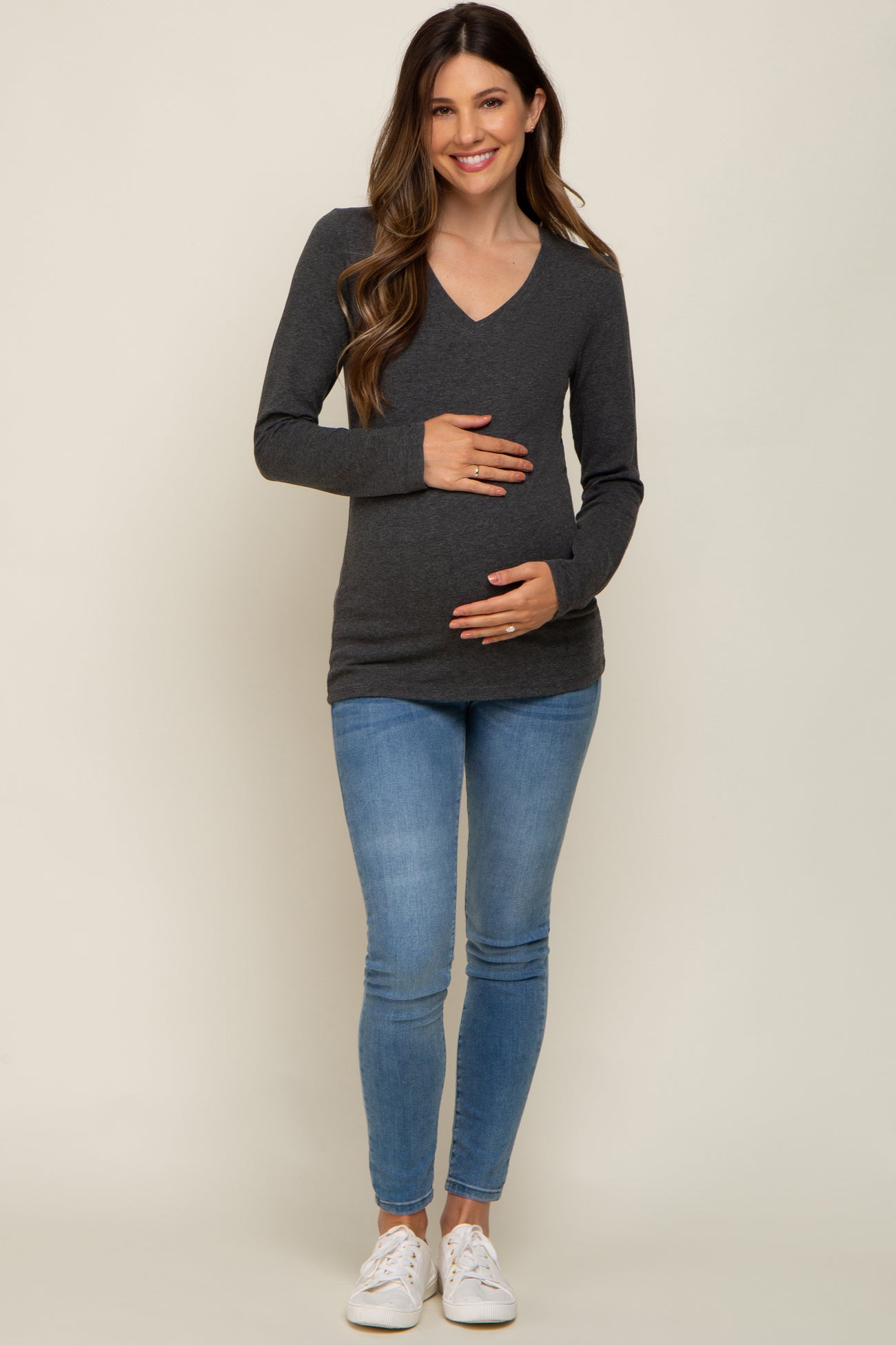 smiling pregnant woman in charcoal v-neck maternity top and blue jeans holding her baby bump