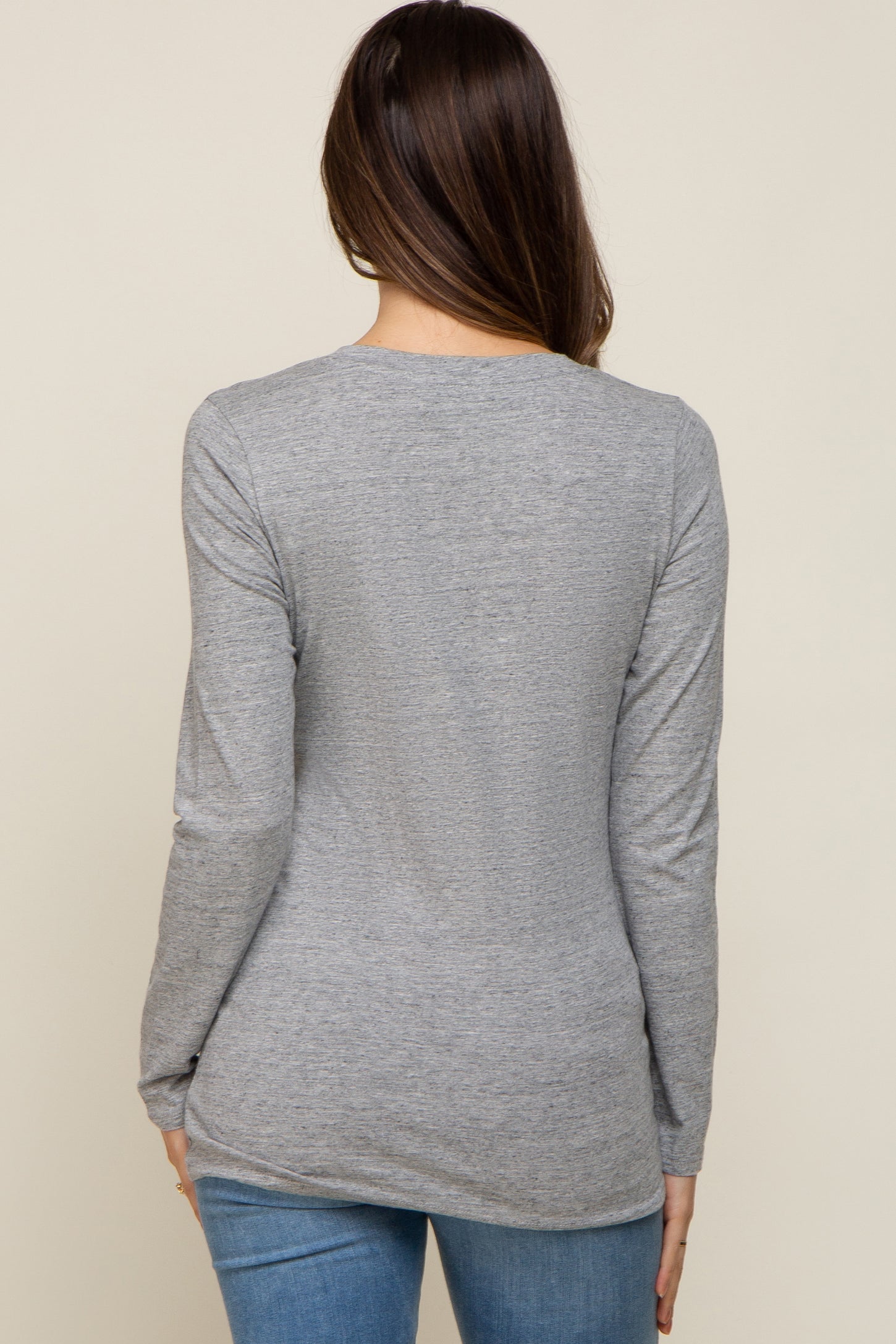 woman wearing a gray long sleeve maternity top from the back, paired with blue jeans