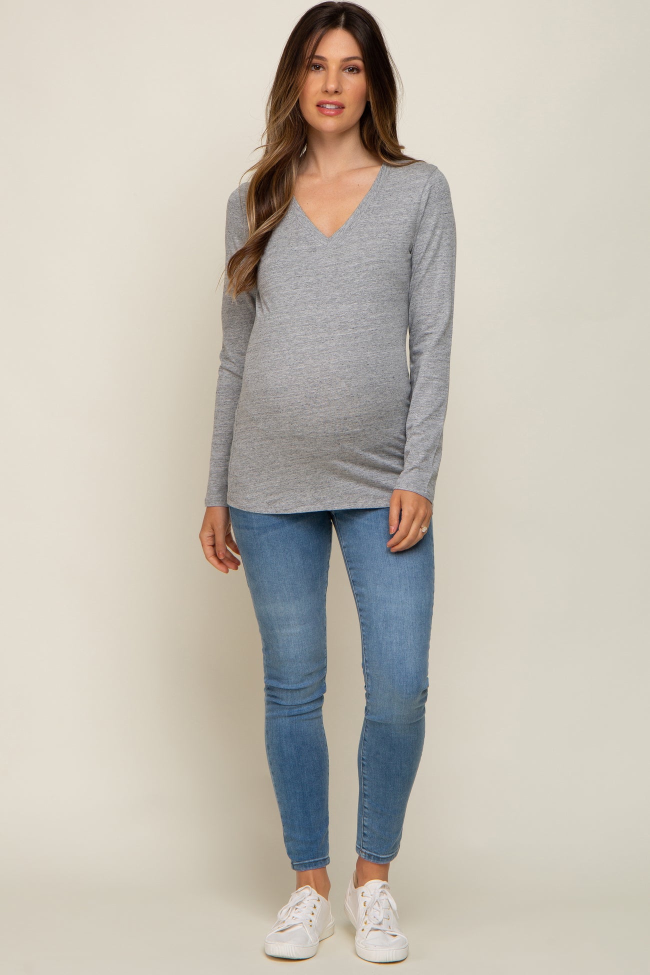 woman wearing a gray maternity long sleeve v-neck top and fitted jeans, showcasing her baby bump