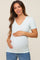 woman wearing a light mint green short sleeve maternity top and gently holding her baby bump