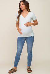 woman wearing a light green v-neck maternity shirt and blue jeans, cradling her baby bump