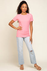 woman wearing a pink short sleeve t-shirt and light wash distressed jeans, standing with one hand on her hip