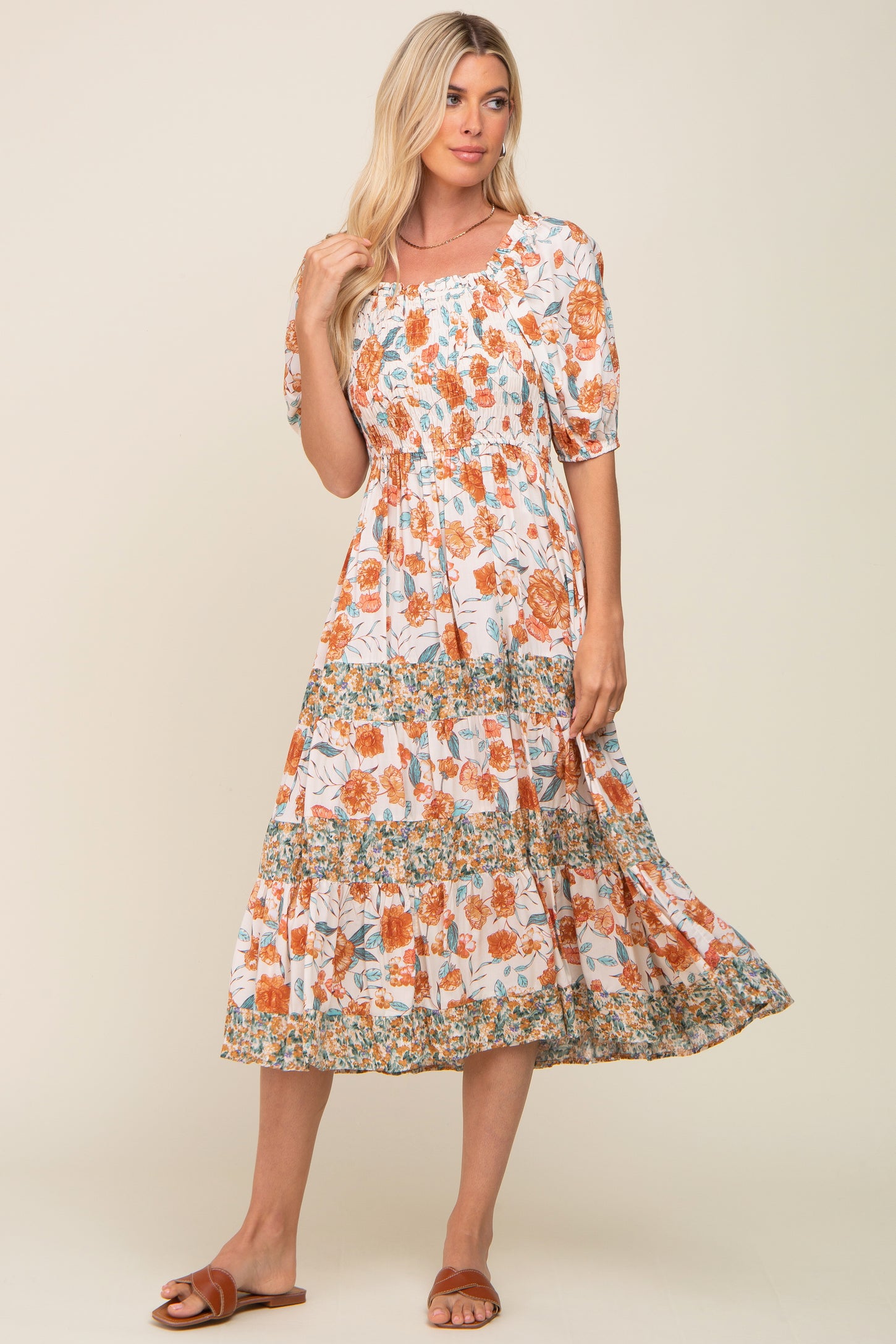 blonde woman wearing a white smocked midi dress with orange floral print and tiered skirt