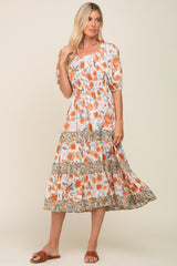 blonde woman wearing a white smocked midi dress with orange floral print and tiered skirt
