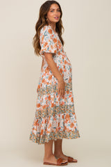 Pregnant woman wearing a floral tiered maternity midi dress with puff sleeves and orange flower print