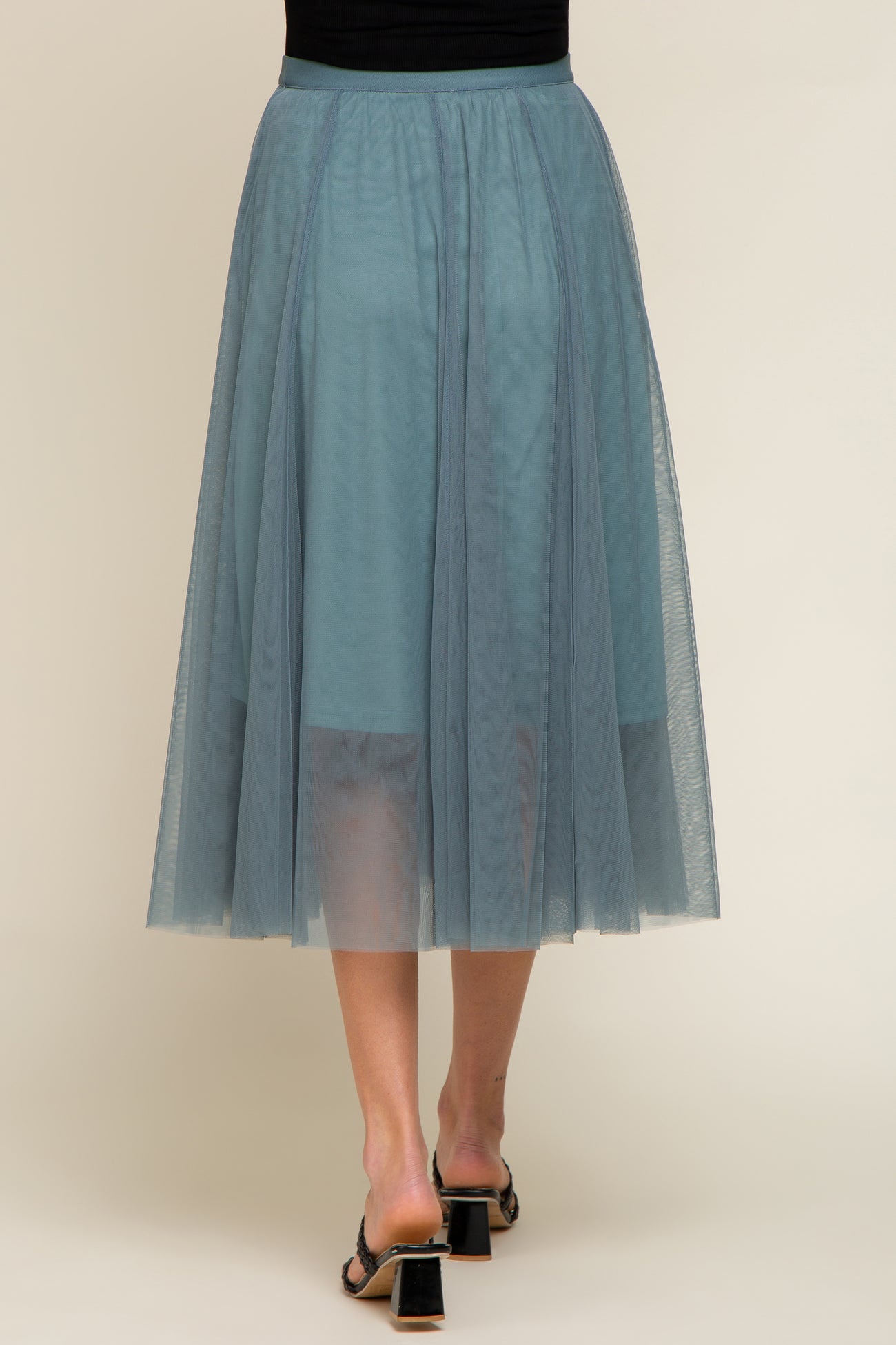 woman wearing a long teal tulle maternity skirt, showing the flowy design and sheer layers from the back