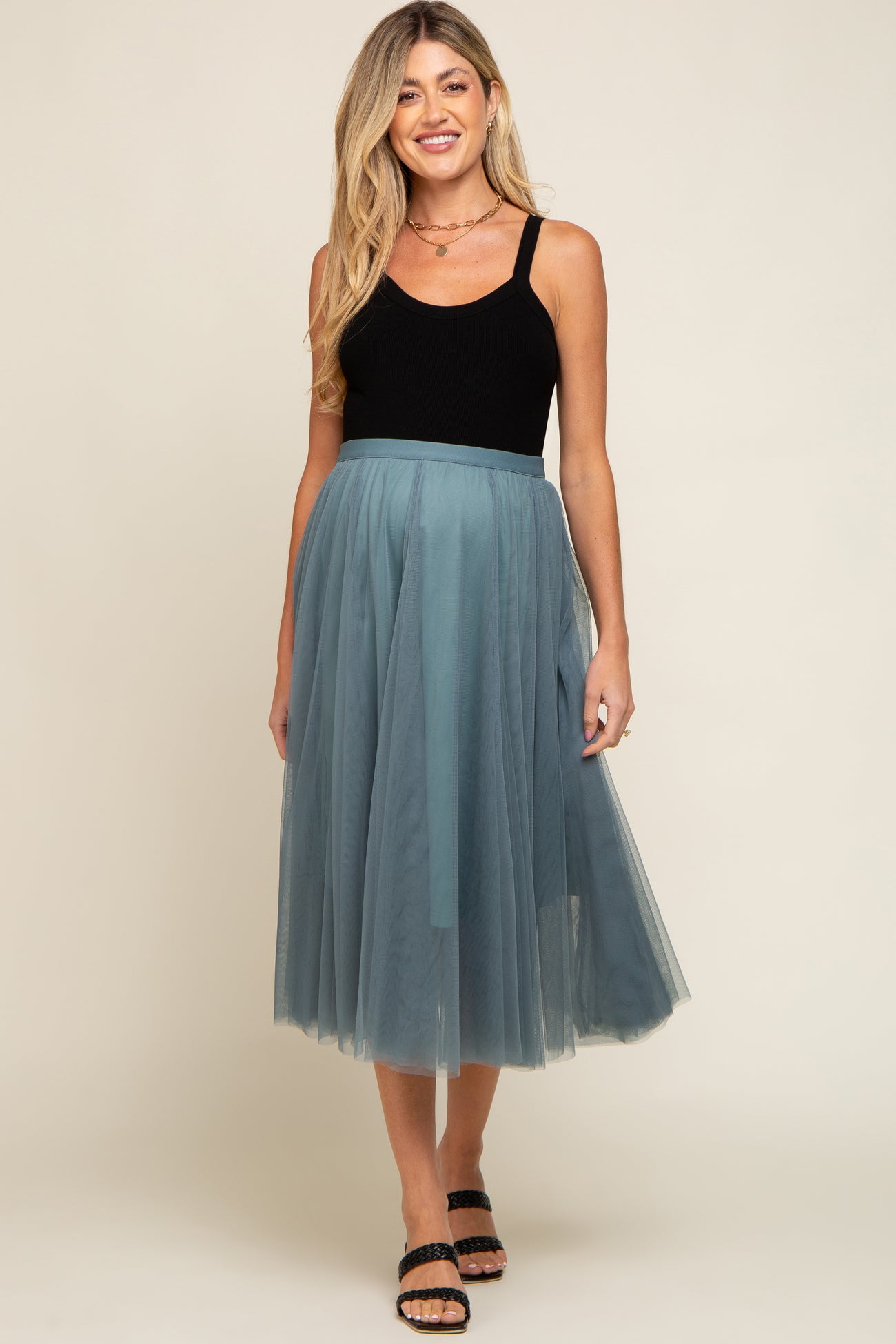 woman wearing a black maternity tank top and a teal tulle midi skirt, standing with a relaxed pose