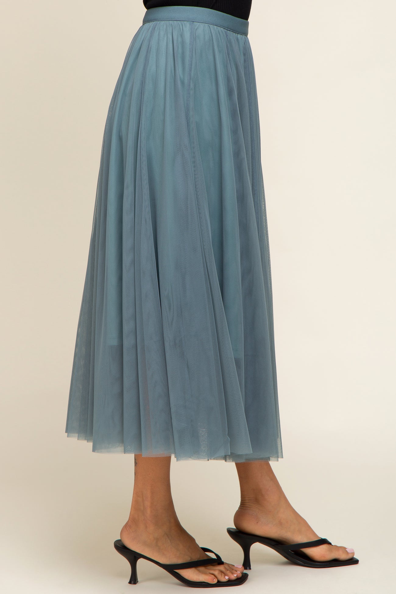 woman wearing a sheer light blue midi tulle skirt with a flowy silhouette and strappy black heeled sandals