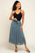 woman wearing a black button-up tank top and a teal tulle maxi skirt, holding sunglasses in her hand
