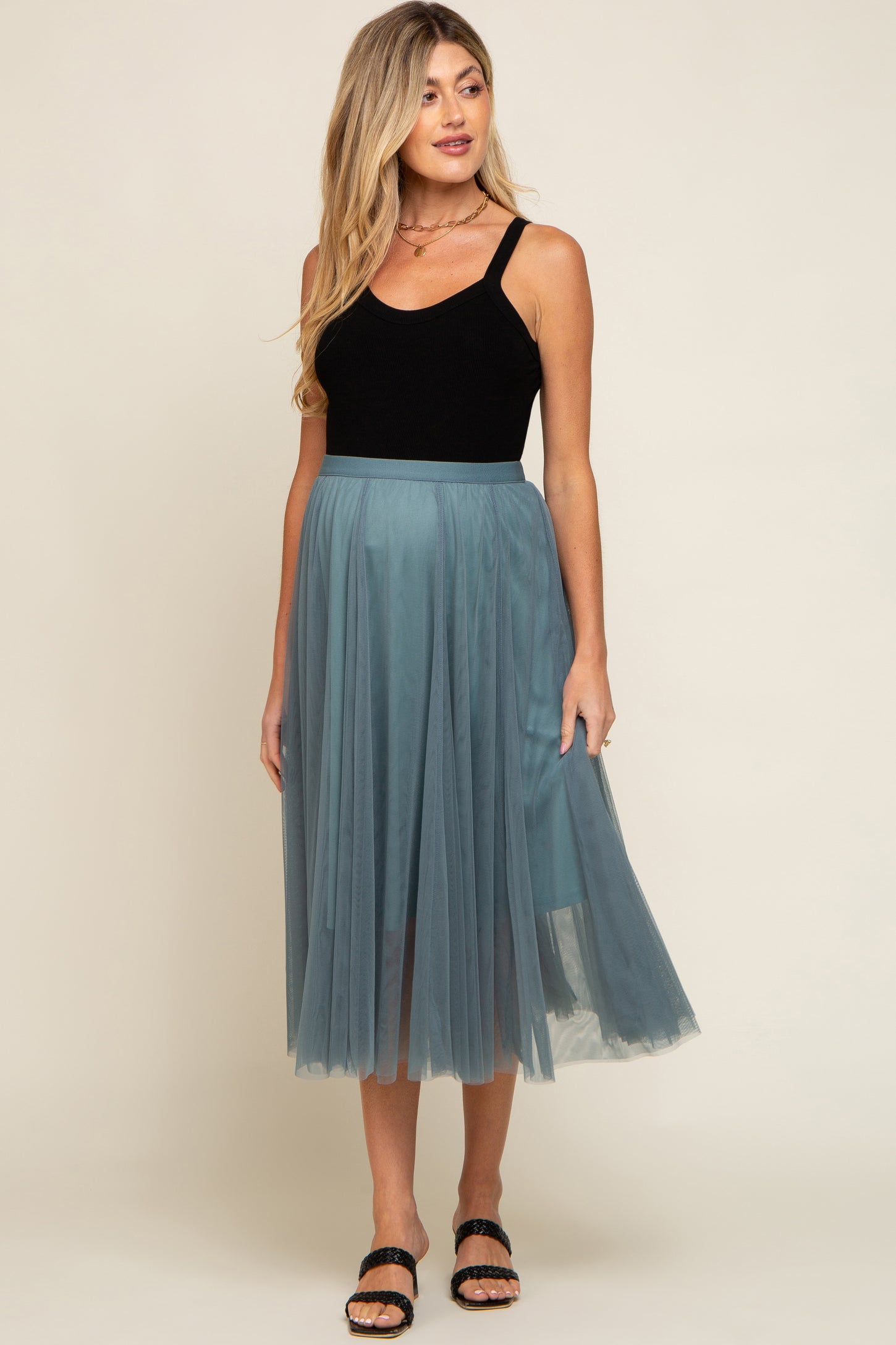 woman wearing a black tank top and a teal tulle maternity skirt, with a flowing design and a relaxed fit