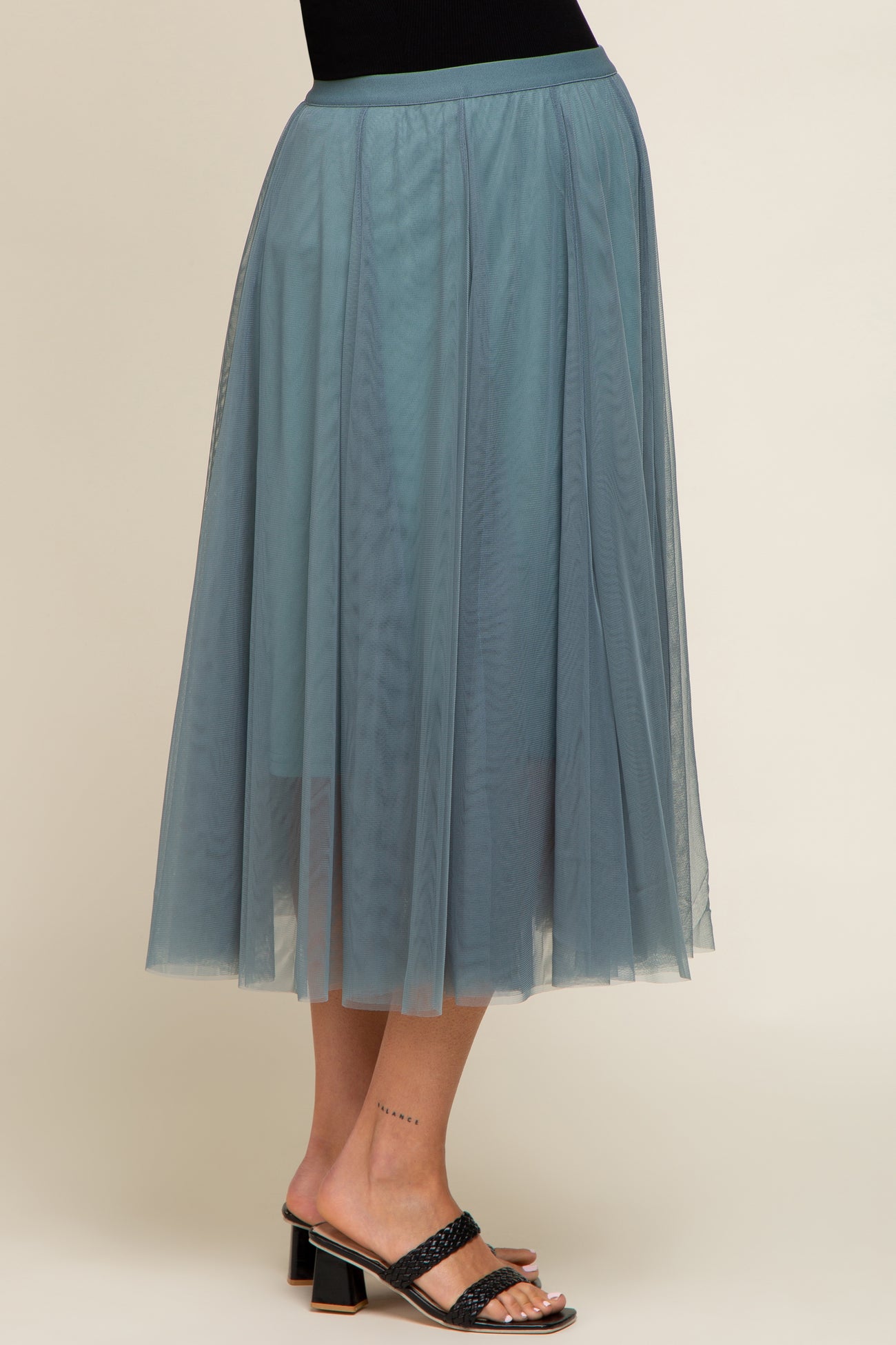 woman wearing a sheer dusty blue maternity skirt with a flowy silhouette and elastic waist, showcasing a baby bump