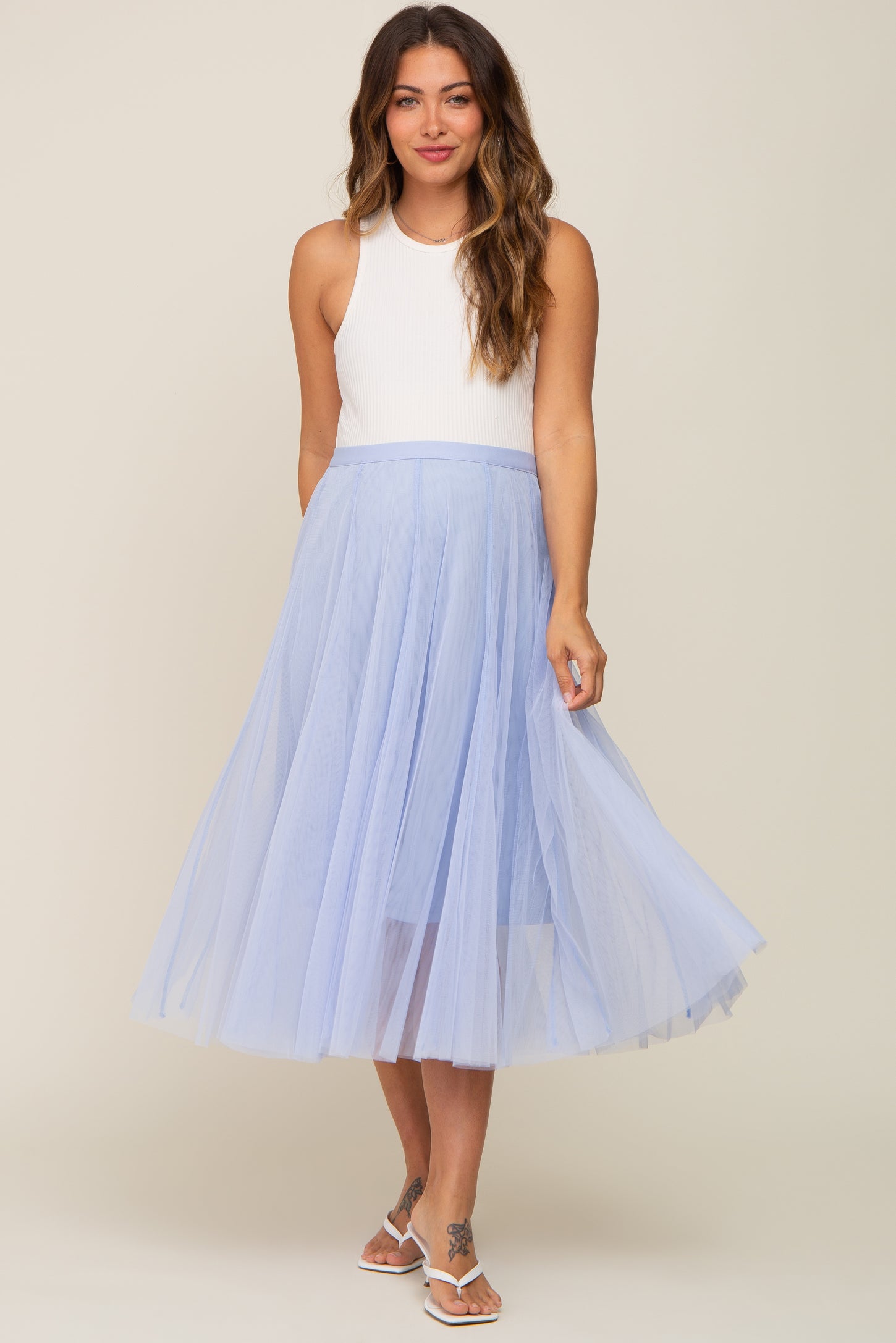 woman wearing a light blue maternity tulle skirt with a white sleeveless top and smiling