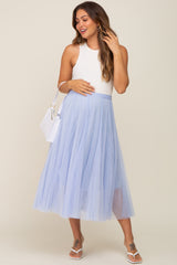 Pregnant woman wearing a white ribbed tank top and light blue tulle midi skirt with a white handbag