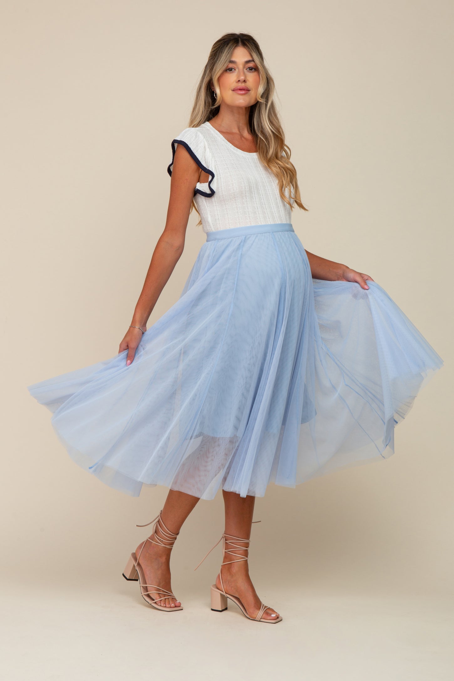 woman wearing a white maternity top with ruffles and a light blue tulle maternity skirt, showing her baby bump