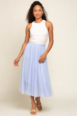 woman wearing a white sleeveless top and a light blue tulle midi skirt, standing and smiling