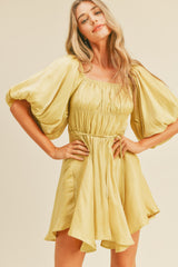 woman wearing a light yellow puff sleeve mini dress with a smocked bodice and a tie waist