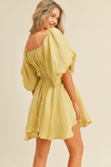 woman wearing a yellow puff sleeve mini dress, smiling and looking back at the camera