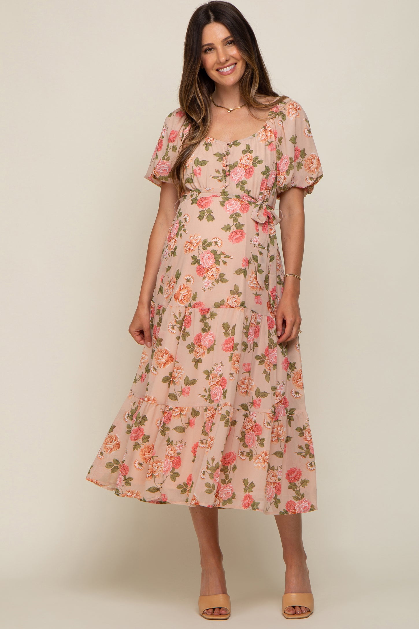 woman wearing a floral print maternity dress with puff sleeves and a tiered skirt, smiling at the camera