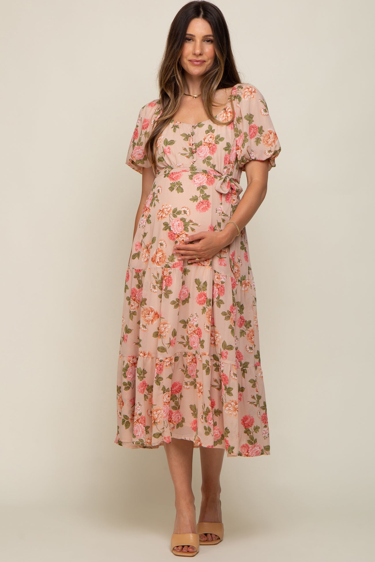 woman wearing a pink floral maternity dress with short puff sleeves and a tied waist, holding her baby bump