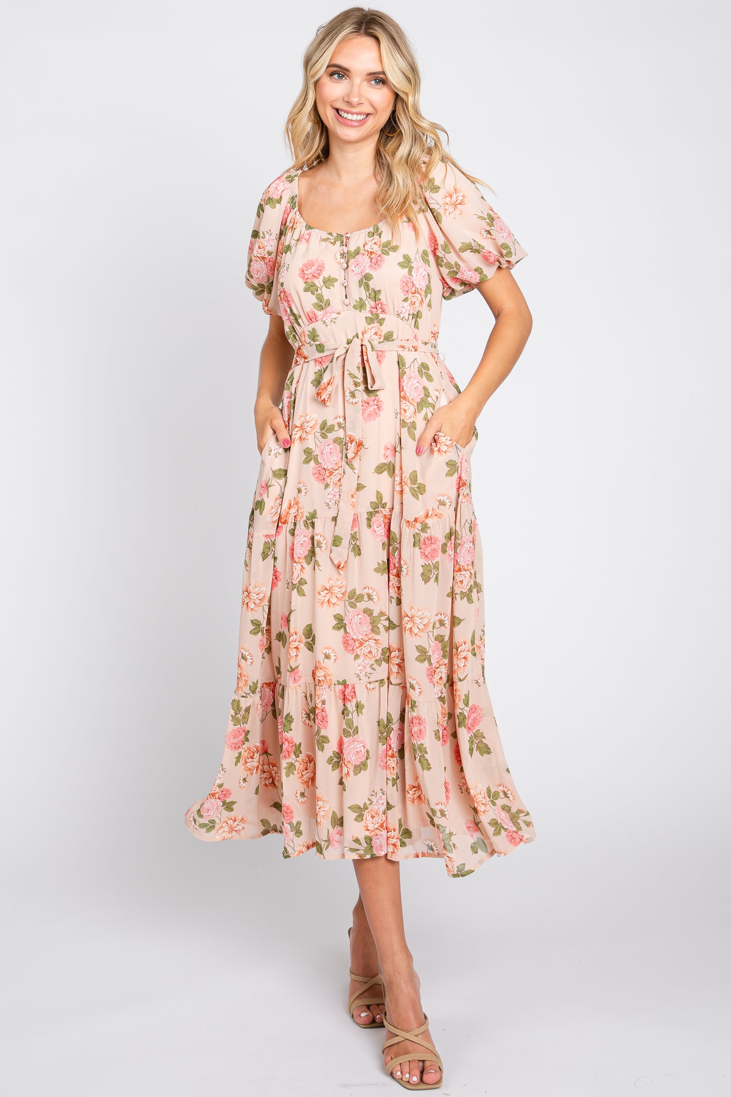 Woman wearing a blush pink floral midi dress with puff sleeves and a tie waist against a white background