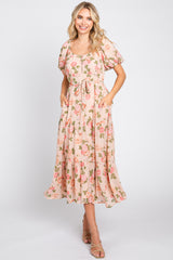 Woman wearing a blush pink floral midi dress with puff sleeves and a tie waist against a white background