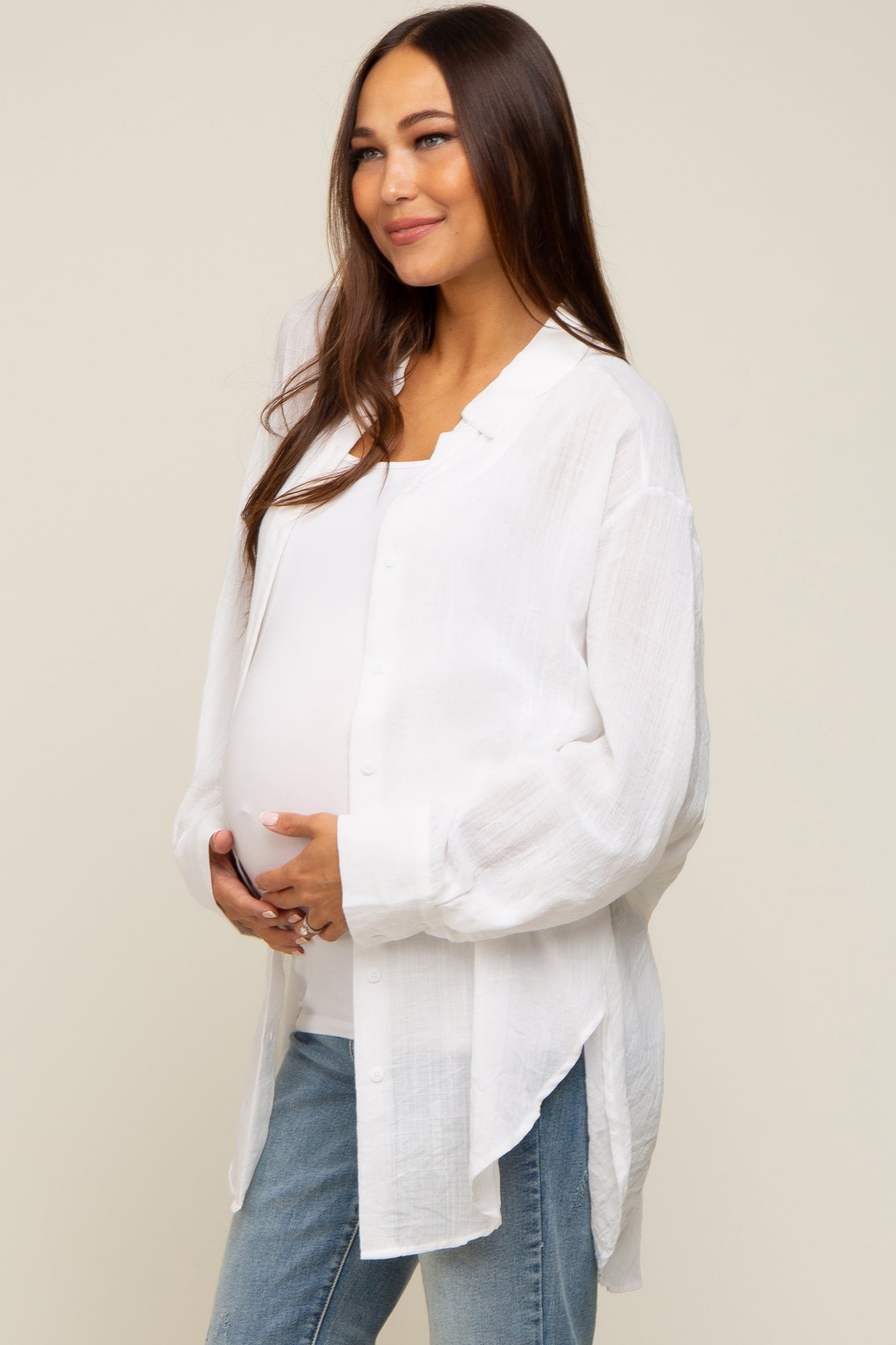 woman wearing a white button-up maternity shirt and blue jeans, holding her baby bump