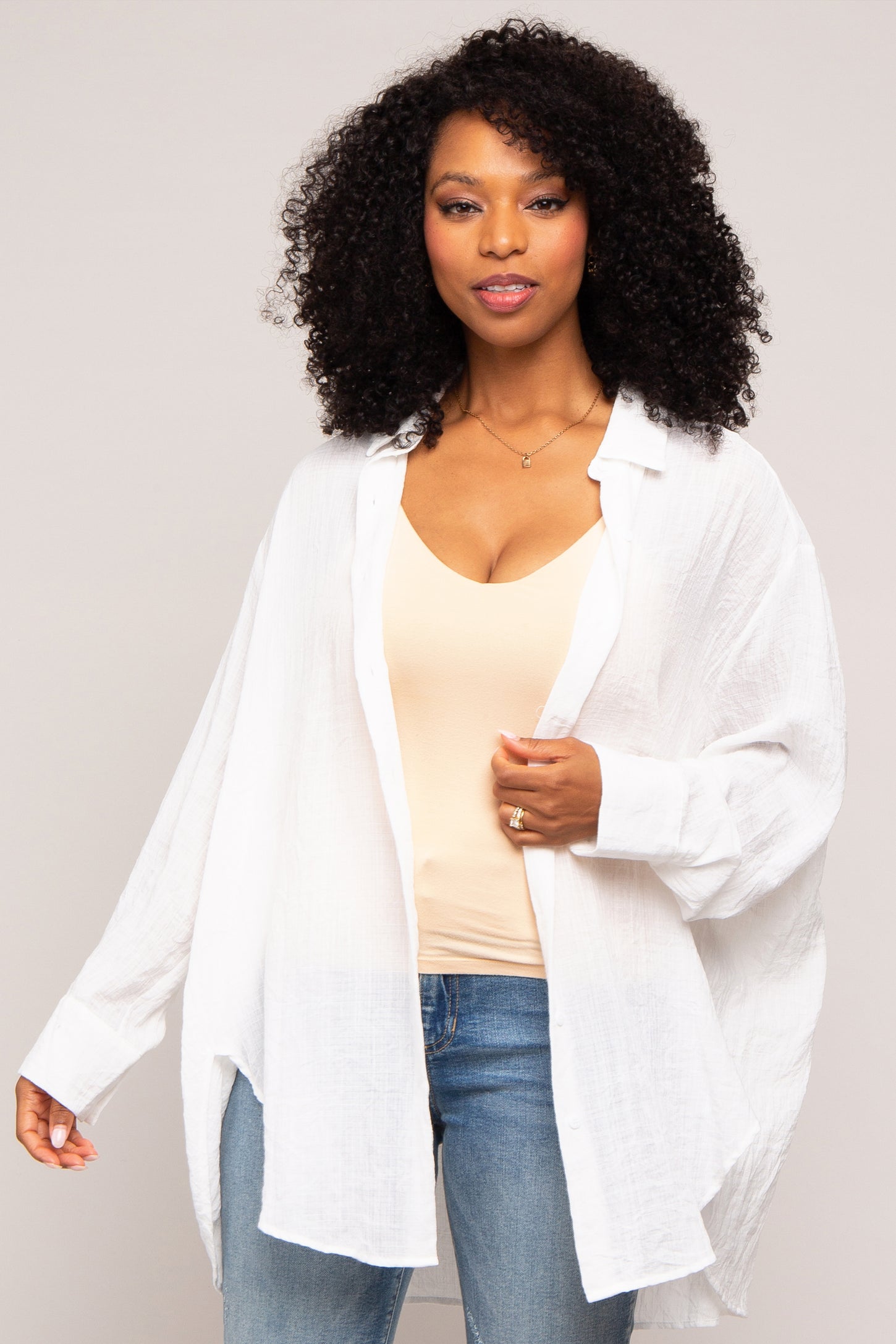 woman wearing a white oversized button-up shirt over a beige tank top and blue jeans