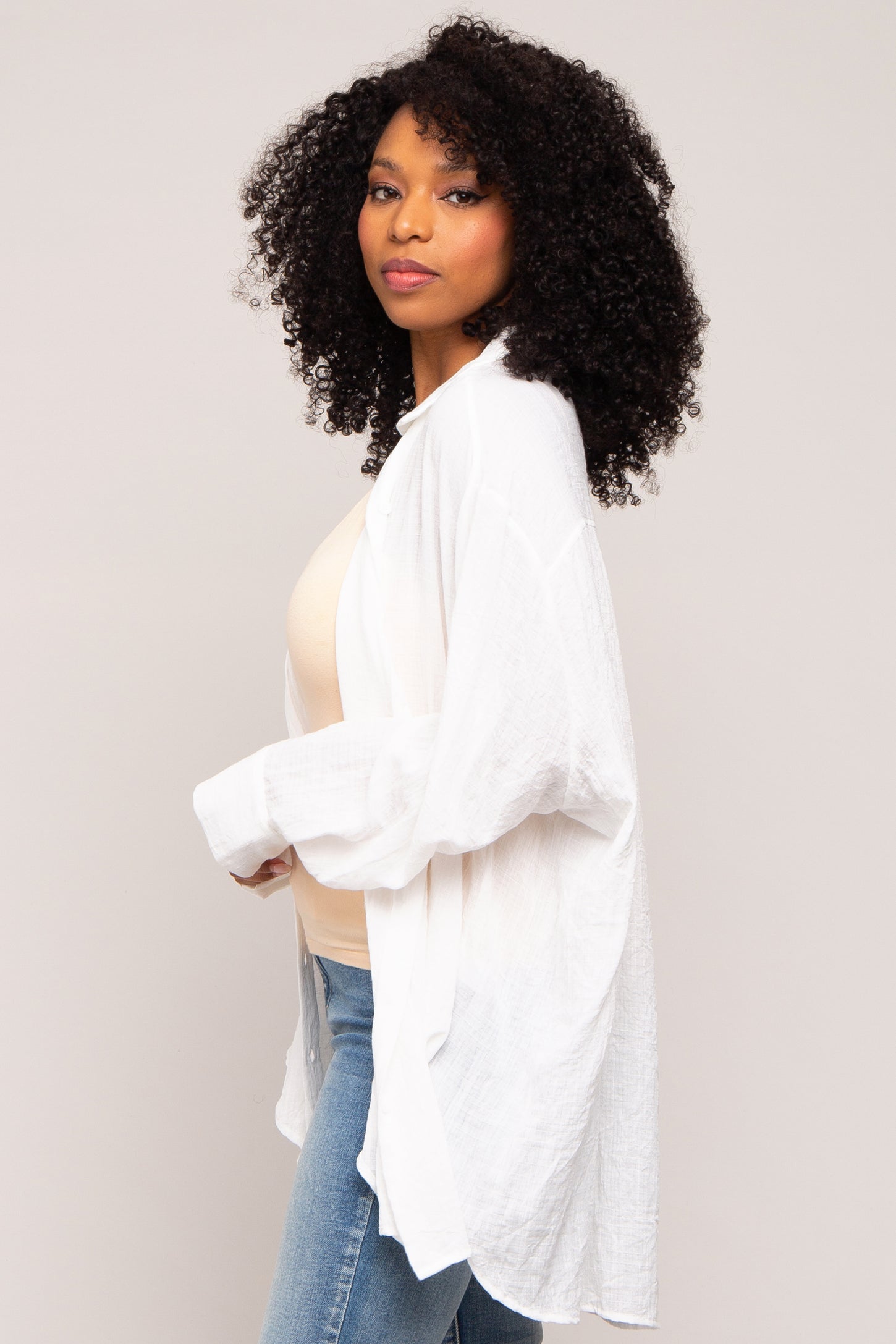 woman wearing a white loose-fitting linen cardigan over a beige top and blue jeans
