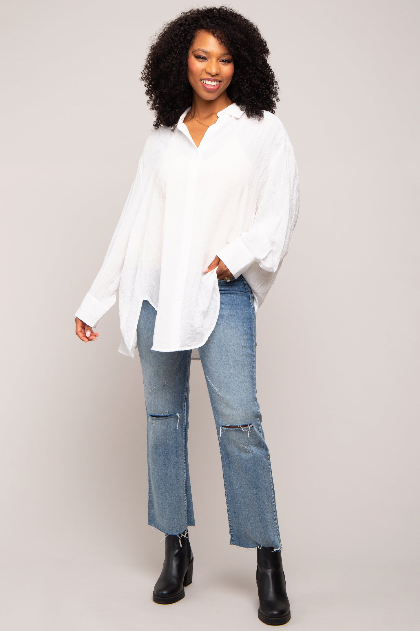 woman wearing a white oversized button-up shirt paired with distressed blue jeans and black ankle boots