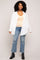 woman wearing an oversized white button-up shirt over a beige tank top and paired with distressed light blue jeans and black heeled boots
