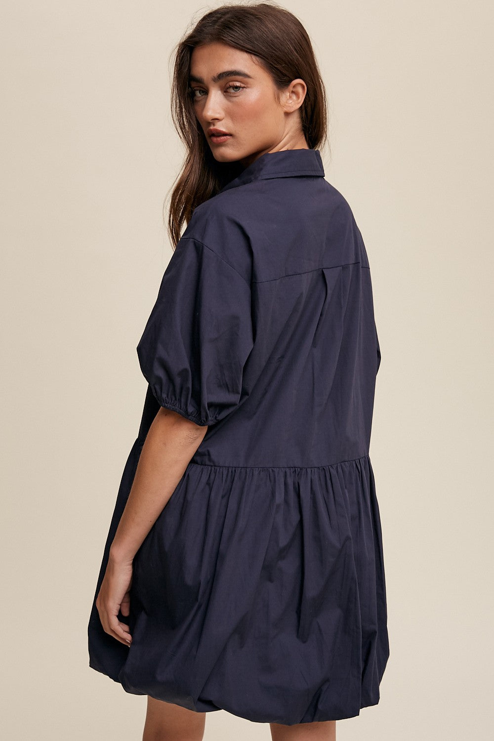 Woman wearing a navy blue puff sleeve babydoll dress with a collared neckline and tiered skirt