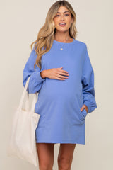 woman wearing a light blue maternity sweatshirt dress and holding her baby bump with a tote bag