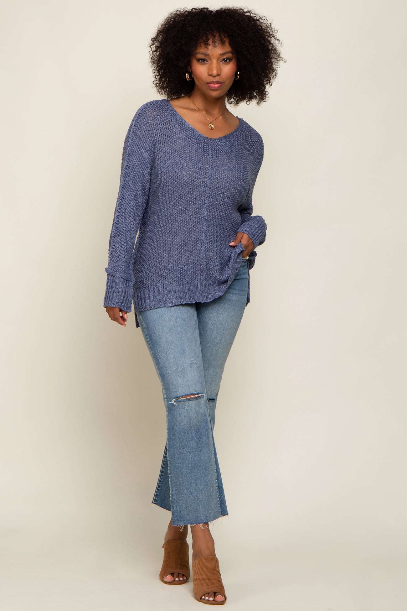 woman wearing a casual blue long sleeve sweater with a v-neck and side slits paired with light wash flared jeans and tan heeled mules
