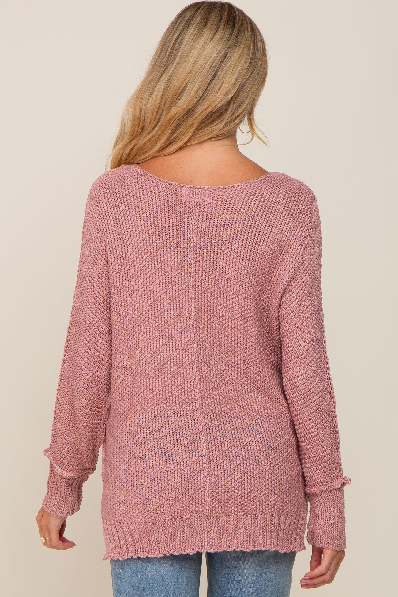 back view of a woman with blonde hair wearing a mauve pink oversized knit sweater and blue jeans
