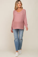 woman wearing a light pink oversized maternity sweater and distressed jeans, showing her baby bump.